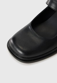 Black leather Mary Jane shoe with square toe and strap, shown on plain light background.