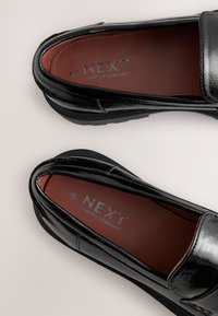 Black synthetic loafers with a glossy finish, rubber soles, and brown insoles featuring embossed "NEXT FOREVER COMFORT" branding.