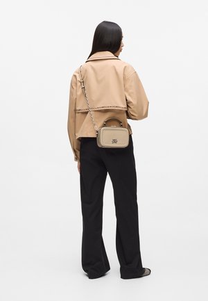 Veste beige courte avec un ourlet orné de chaînes, associée à un pantalon noir à jambes larges. Un petit sac à main crème avec une anse et une bandoulière.
