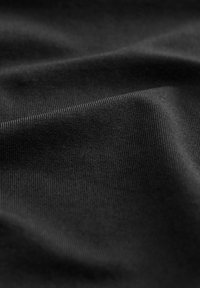 Schwarzer Stoff mit einer glatten, geriffelten Textur, der subtile Falten und unterschiedliche Lichtreflexionen aufweist, die auf ein weiches, elastisches Material hinweisen.