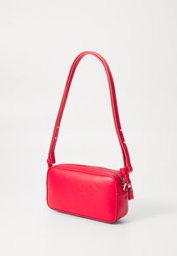 Sac bandoulière en cuir rouge de forme rectangulaire, avec fermeture éclair et sangle réglable. Texture lisse et design minimaliste.