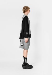 Conjunto deportivo que incluye una sudadera en capas negra y gris, pantalones cortos grises, zuecos texturizados negros y calcetines deportivos negros con letras blancas.