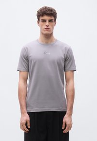 Γκρι κοντομάνικη μπλούζα με στρογγυλή λαιμόκοψη, κατ�ασκευασμένη από απαλό ύφασμα. Διαθέτει διακριτικό λογότυπο "BOSS" στο στήθος, σε συνδυασμό με μαύρο φαρδύ παντελόνι.