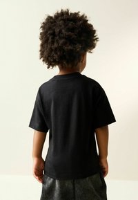 Black cotton t-shirt with short sleeves and a round neck, viewed from the back. Soft texture and simple design with no visible logos or patterns.