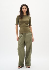 Olivgrünes, geripptes Kurzarmoberteil, kombiniert mit lockeren olivgrünen Hosen. Beide Kleidungsstücke besitzen eine glatte Textur und ein minimalistisches Design.