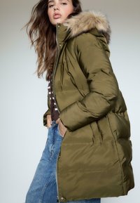 Oliwkowa puchowa kurtka z kapturem z sztucznego futra, zapinana na zamek, z elastycznymi mankietami; posiada teksturowany wzór pikowania oraz boczne kieszenie.
