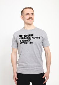 Šedé bavlněné tričko s krátkým rukávem, na kterém je tučný černý nápis: "MOJE NEJLEPŠÍ DĚTSKÁ VZPOMÍNKA JE, ŽE MNOU NEBOLÍ ZÁDA." Jednoduchý design.