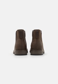 Bottines en cuir marron avec une texture lisse, présentant un talon renforcé, une semelle empilée basse et des détails de couture minimalistes.
