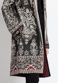 Knælang uldfrakke med et sort og hvidt geometrisk mønster, røde accenter, to frontlommer og lynlås lukning. Struktureret strikket stof.