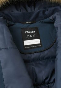 Interno della giacca isolante blu navy, con un'etichetta nera che presenta simboli di manutenzione e informazioni sulla taglia, enfatizzando il design sostenibile dalla Finlandia.