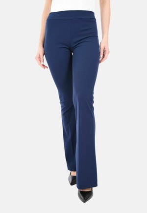 Donna che indossa pantaloni a zampa d'elefante blu navy attillati, abbinati a scarpe nere con punta a colore, mostrata dalla vita ai piedi.