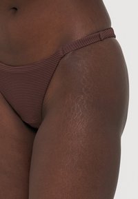 Brun ribbet bikini-bunn med tynne sidestrikker, som har et sømløst design som forbedrer komforten og gir en subtil tekstur.