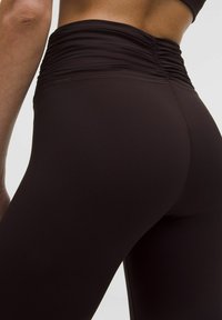 Leggings cu talie înaltă, ajustate, dintr-un material maroniu închis, cu un tiv strâns și o textură netedă. Fără modele vizibile sau accesorii.