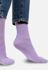 Jasnofioletowe skarpetki do kostek z ryflowanym wzorem, o gładkiej fakturze, ułożone razem z dżinsami lekko podwiniętymi na brzegu.