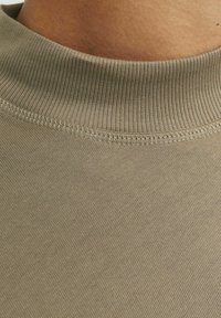 Svetlo olivno zeleni bombažni majica s kratkimi rokavi z rebrastim ovratnikom, gladko teksturo in minimalnim šivom ob robu ovratnika.
