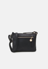 Sac à bandoulière en cuir noir avec une texture lisse, des compartiments zippés, un accent en métal doré et un charm détachable.