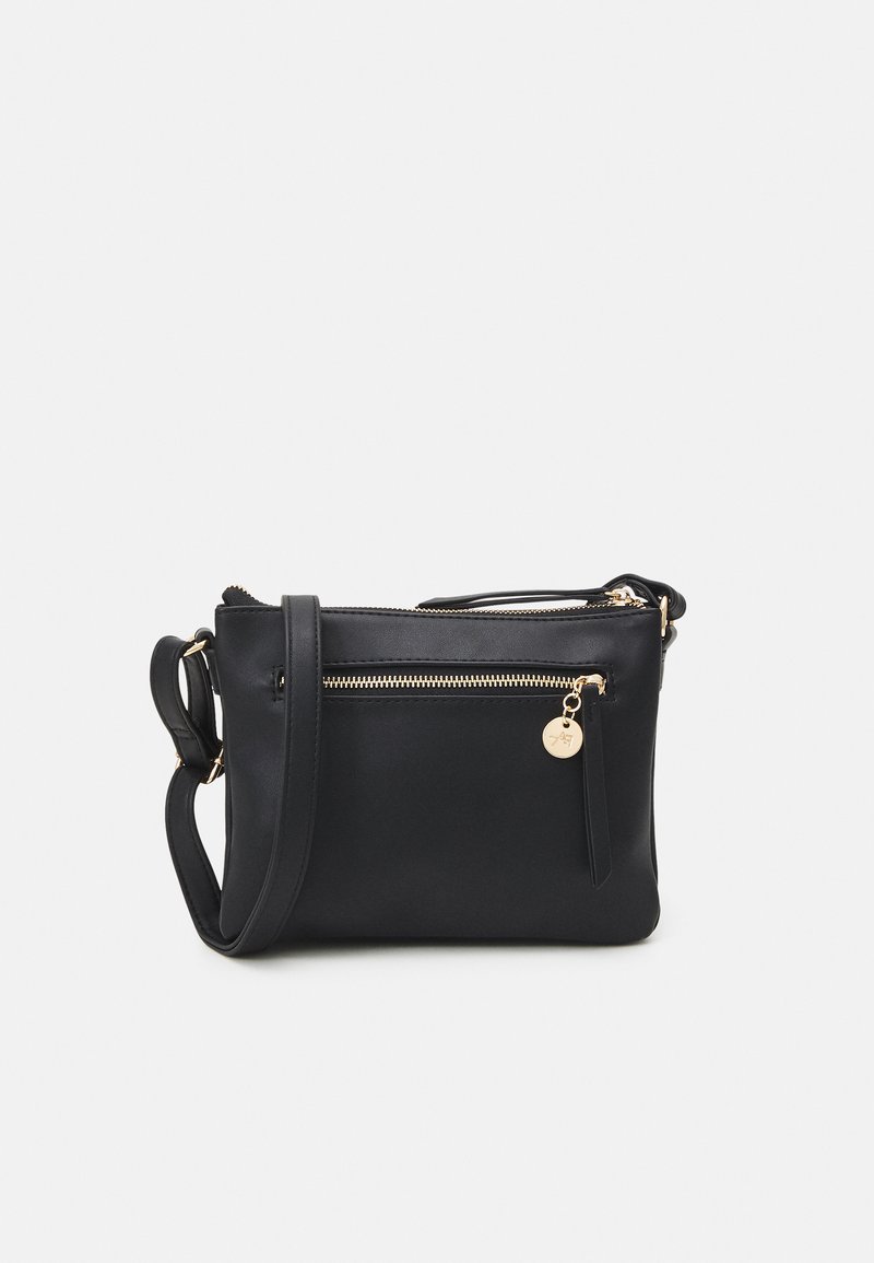 Sac à bandoulière en cuir noir avec une texture lisse, des compartiments zippés, un accent en métal doré et un charm détachable.