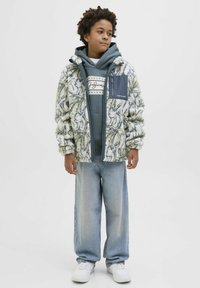 Chaqueta blanca esponjosa con un patrón floral amarillo y verde, superpuesta a una sudadera gris, combinada con unos pantalones vaqueros de pierna ancha de color azul claro y zapatillas blancas.