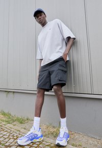 Grå oversized t-skjorte, svarte cargo-shorts med sidelommer, hvite ankelsokker og blå/hvite sneakers med detaljer. Minimalistisk design.
