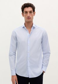Camisa de manga larga azul claro hecha de algodón, con collar abotonado, textura sutil y botones en contraste.