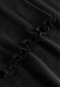 Melnas tekstila audums ar horizontālu volānu rakstu vidū, ar teksturētu virsmu un smalkām dimanta motīvām audumā.