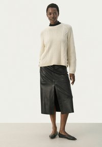 Cremefarvet strikket sweater med teksturerede mønstre, parret med en sort læder midi-nederdel med en frontspalte. Sorte flade sko fuldender looket.