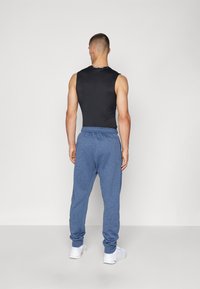 Sort ærmeløs top parret med blå atletiske joggers og hvide sneakers. Joggersne har snor i taljen og ribbede manchetter.