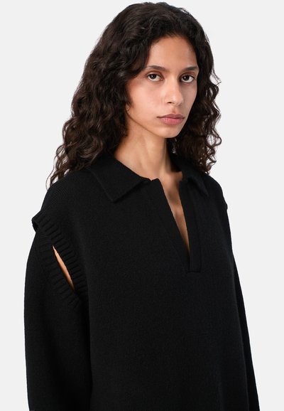 Przesadnie duży czarny sweter z dzianiny, z kołnierzem, głębokim dekoltem V oraz prążkowanymi akcentami wokół otworów na ramiona, podkreślający swoją teksturę i wzornictwo.