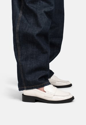 Witte leren loafers met zwarte zolen, gedragen bij donkerblauwe spijkerbroeken, net boven de schoenen ingekort.