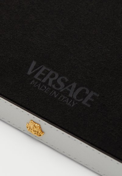 Juodas veltinio dėklas su iškilniu "VERSACE MADE IN ITALY" logotipu; turi auksinius priedus ir baltus siūlus pilkuose šonuose.