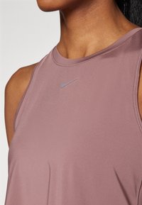 Top atletico senza maniche di colore viola con una texture liscia, caratterizzato da un discreto logo Nike grigio sul petto e da un collo rotondo.