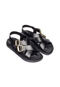 Schwarze Ledersandalen mit überkreuzten Riemen, goldenen Schnallen, einer flachen Sohle und einer glatten Textur. Keine Muster oder Verzierungen.