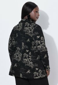 Černý texturovaný blazer s propracovanými zlatými květinovými a krajinovými vzory. Obsahuje klopový límec a knoflíkové detaily na manžetách.