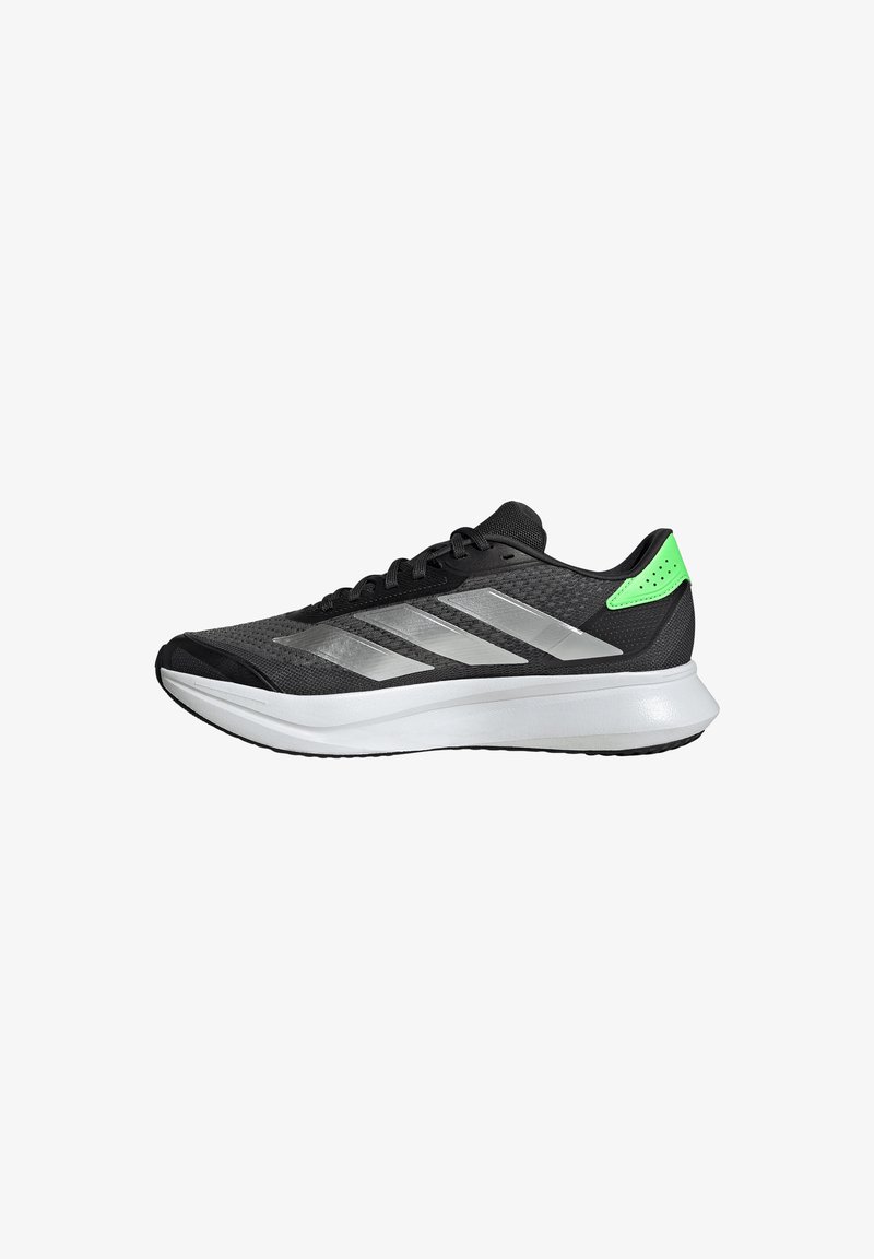 Chaussure de course noire et verte avec semelle blanche et rayures argentées, vue de côté sur fond blanc.