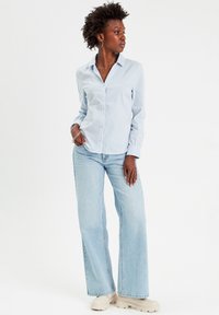 Chemise à boutons bleue claire avec des rayures verticales blanches, associée à un jean large bleu clair et des chaussures à plateforme beiges.