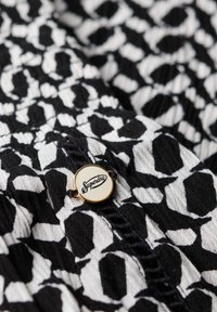 Top en blanco y negro con un patrón de estampado de leopardo, tejido texturizado y una etiqueta circular dorada que dice "Superdry."