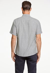 Korte mouwen, geknoopte shirt van een grijze linnenmix. Heeft een gebogen zoom en subtiele textuur. Achteraan zijn de knoopsluiting en stikdetails zichtbaar.