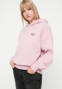 Roosa kapuutsiga särk, mis on valmistatud pehmest materjalist, millel on ees tasku ja väike tumesinise värviga tikand vasakul rinnal.