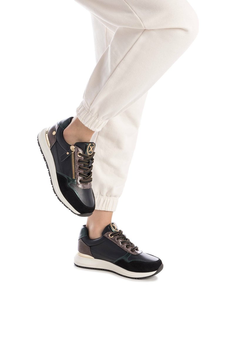 Zapatillas deportivas con parte superior de cuero negro y verde, acentos metálicos y una cremallera dorada. Suela blanca con agarre texturizado.