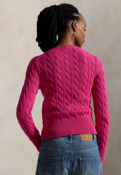 Φούξια πουλόβερ με πλέξη καλωδίου και ριμπ τελείωμα στα μανίκια και τη μέση. Φορώντας το με μπλέ τζιν ψηλόμεσα με δερμάτινο λογότυπο του brand.