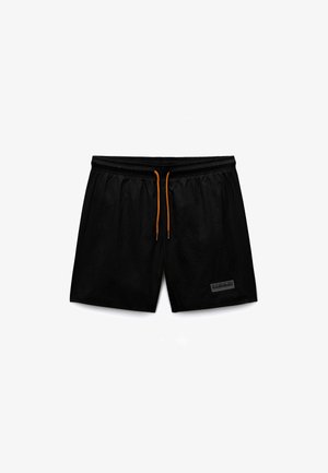 Pantalones cortos deportivos negros para hombre con cordón naranja y un pequeño parche rectangular con logo en la parte inferior de la pierna izquierda.