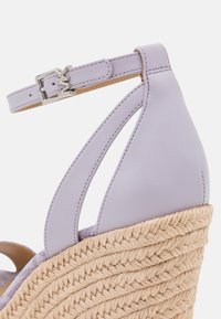 Sandale compensée en cuir lilas avec bride à la cheville, boucle argentée et semelle tressée en fibres naturelles.