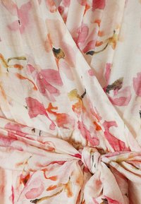 Blødt stof med lyserødt, orange og gult blomsterprint bundet i en knude ved taljen, der viser en samlet og overlappende tekstur.