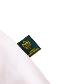 Witte stof met een gestructureerde weving, voorzien van een groene label met gouden accenten waarop "AS ROMA OFFICIAL PRODUCT" en een schildlogo is afgebeeld.