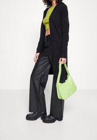 Czarny długi kardigan, zielony krótki top, czarne skórzane spodnie o szerokich nogawkach oraz błyszcząca zielona torebka; masywne czarne buty na platformie.