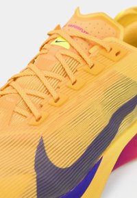 Nike Vaporfly tenisice u jarko narančastoj boji s teksturiranom tkaninom, ljubičastim i plavim akcentima, istaknutim sustavom vezanja i laganim dizajnom.