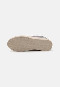Calvin Klein sneaker alsó nézete, világos bézs gumitalppal, amely texturált mintával és márkázással rendelkezik, fehér háttér előtt.