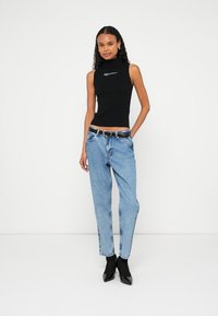 Top preto sem mangas com gola alta, combinado com jeans azul-claro de perna reta. A modelo usa um cinto preto e sapatos de salto alto pretos com bico apontado.