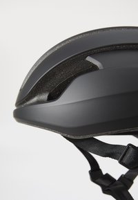 Czarny kask rowerowy o gładkiej powierzchni, aerodynamicznym kształcie, wentylacyjnych otworach i teksturowanym pasku umożliwiającym pewne dopasowanie.