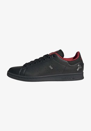 Baskets basses noires avec doublure intérieure rouge, panneau latéral perforé portant l'inscription "THOR" et symbole du marteau de Thor près du talon.